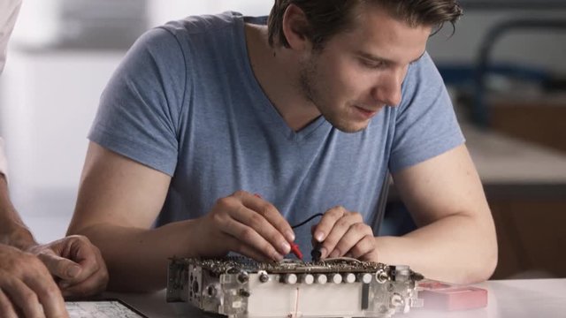 Young trainee testing solder points on old radio after reading construction manuell on tablet; close up