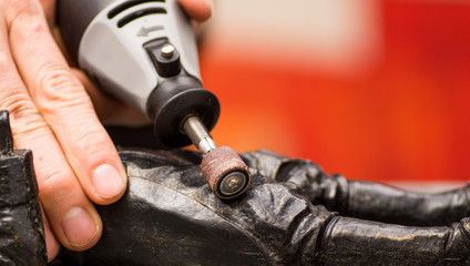 Closeup of a hardworker man using a polisher over a metallic statue on a blurred background