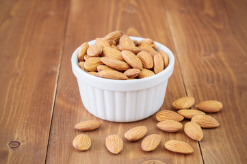 Almonds nuts in white bowl on wooden background