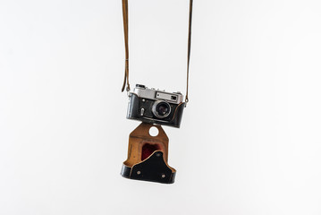 Vintage film camera in a leather case hanging on straps on a white background