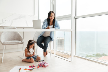 Concentrated woman write notes while her daughter sitting on floor.