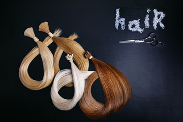 hair extensions of four colors on a dark background with scissors. copyspace. top view.