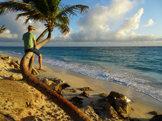 Junger Mann auf Palme bei Sonnenaufgang über dem Meer