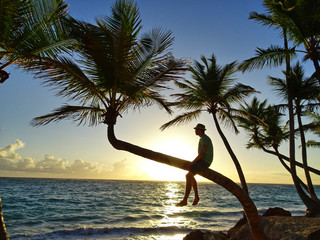 junger Mann auf Palme bei Sonnenaufgang über dem Meer
