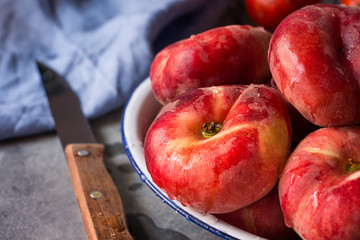Bunch of ripe organic colorful red saturn peaches with water drops on white plate, knife, blue napkin, dark kitchen table, rustic interior © olindana
