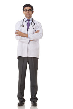 Full length of confident young doctor with hands folded over white background 