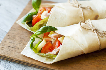 Healthy lunch snack. Tortilla wraps with grilled chicken fillet and fresh vegetables on wooden background. close-up
