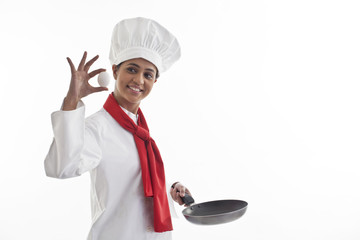 Happy female chef holding an egg and frying pan isolated over white background 