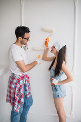 The young joyful couple does repair at home, they paint the wall with help of platens and look at each other