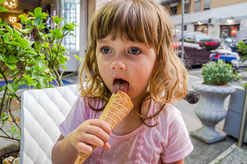 Little charming girl the child eats and licks the languages of gelato in a street cafe in Rome, the capital of Italy