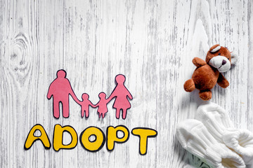 Adopt word, paper silhouette of family and toys on light wooden table background top view copyspace