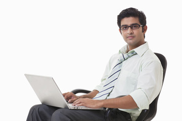 Confident young businessman on chair using laptop 