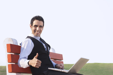 Portrait of businessman with laptop giving thumbs up , INDIA , DELHI