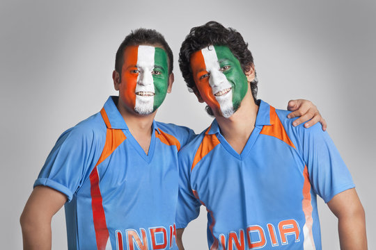Male cricket fans with face painted in tricolor standing together over colored background 