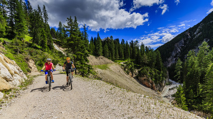 Mountain biking woman and young girl along river in Dolomites, Italy