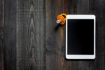 Mockup for adoption concept. Tablet PC near baby pacifier on dark wooden background top view copyspace
