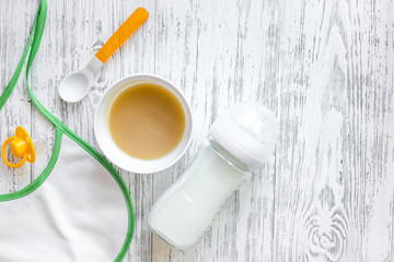 Preparing to feed baby. Puree, spoon, nipple, bottle and bib on light wooden table background top...
