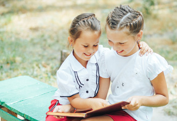 Two girls are reading an interesting book in the park