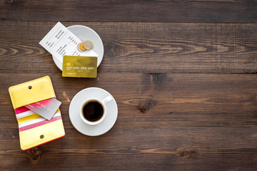 Restaurant bill, purse and bank card near cup of coffee on dark wooden table top view copyspace