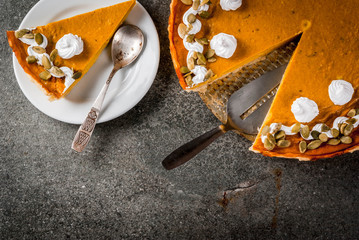 Traditional autumn dishes. Halloween, Thanksgiving. Sliced spicy pumpkin pie with whipped cream & pumpkin seeds on black stone table. Top view copy space