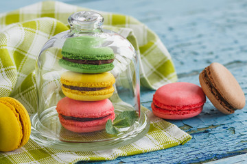 Green, pink and yellow french macarons under the glass on the wooden boards