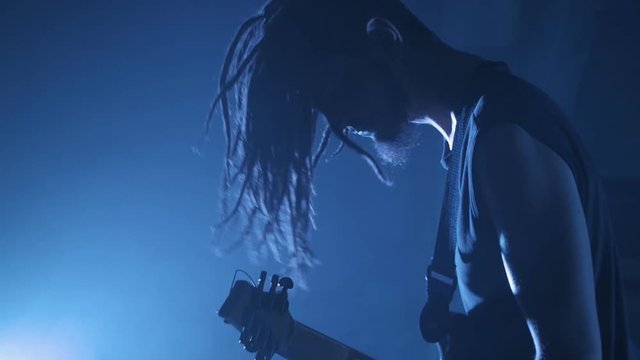 Guitarist rocker with dreadlocks playing the electric guitar on stage. Performance music video rock, punk, heavy metal band in slow motion.