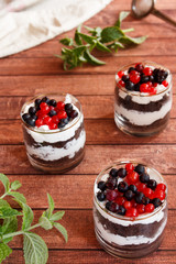 A sweet dessert of sponge cake with cream in a glass with fresh berries on wooden dark background