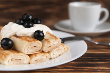 Breakfast. Pancakes on a wooden table with cheese and black currants. In the background a Cup of coffee.