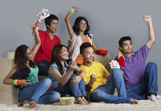 Young friends having a great time together while watching cricket match at home 