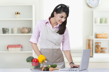 Obraz na płótnie Canvas Businesswoman using laptop while preparing food in kitchen at home