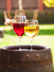 Glasses of red and white wine with grape on old wine barrel outside