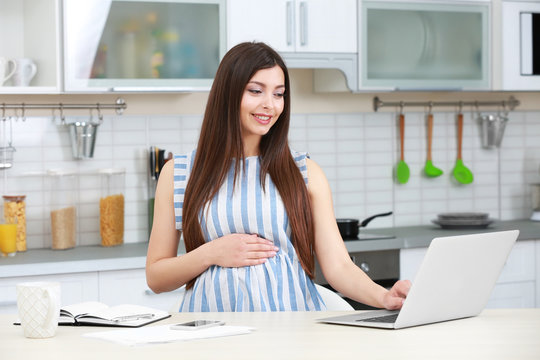 Beautiful young pregnant woman working in kitchen
