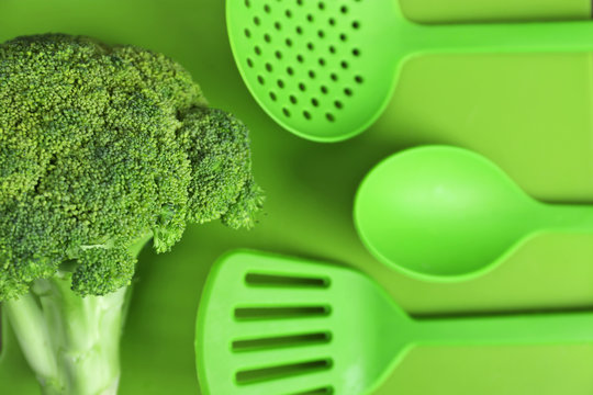 Fresh broccoli and utensils on green background
