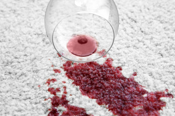 Glass of red wine spilled on white carpet, close up