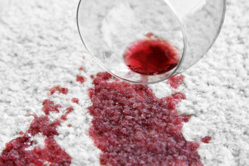 Glass of red wine spilled on white carpet, closeup