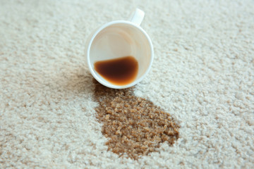 Cup of coffee spilled on white carpet, close up