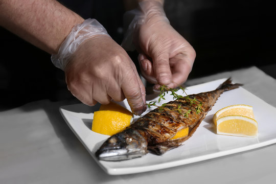 Man putting thyme onto tasty fish with lemon on plate
