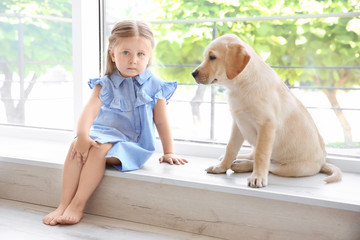 Cute child with labrador retriever on window sill at home