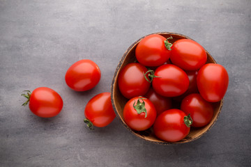 Small plum tomatoes in a wooden bowl on a gray background.