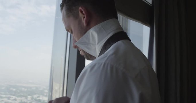 Businessman ties tie in hotel, slow motion