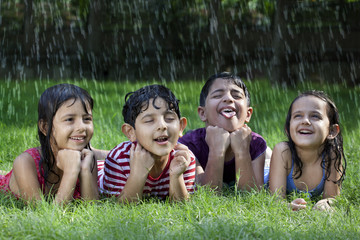 Little boys and girls lying on grass enjoying rain 
