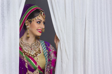 Smiling Indian bride standing amidst curtains