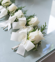 White roses boutonniere with white bow tie ribbon groomsmen on glass table in shadow of light through the window