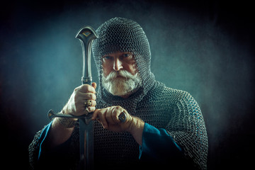 Powerful bearded knight with the sword on the dark background - obrazy, fototapety, plakaty