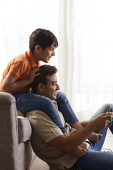 Father playing video game with boy sitting on his shoulder