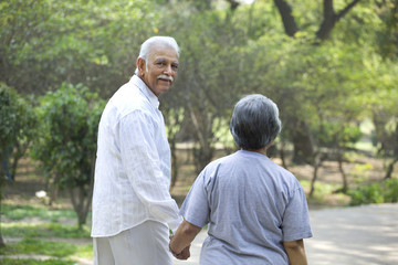 Senior man and woman walking in park while holding hands 