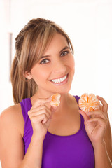 Beautiful young smiling woman wearing a purple-shirt and eating a tangerine in a white background