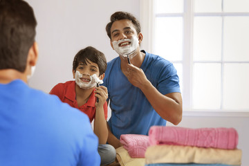 Reflection of father and son shaving with razor in bathroom