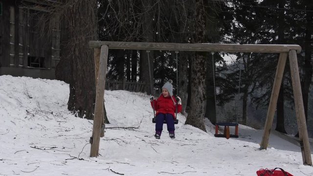 A little girl swinging on the swing while someone throws snowballs on her