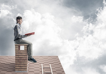 Handsome man on brick roof against cloud scape reading book